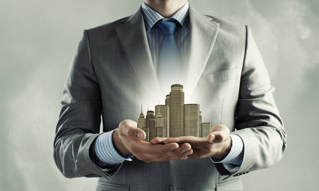 Close up of businessman holding modern office center model in handsの写真素材