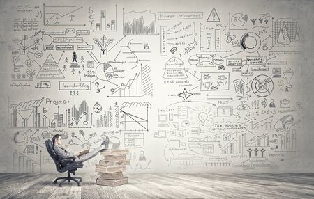 Young handsome businessman sitting in chair with his legs on pile of booksの写真素材