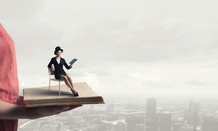 Pretty girl wearing retro hat siting on chair with book in handsの写真素材