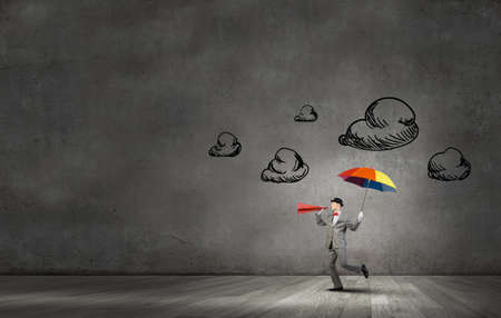 Young businessman with colorful umbrella screaming emotionally in paper trumpetの写真素材