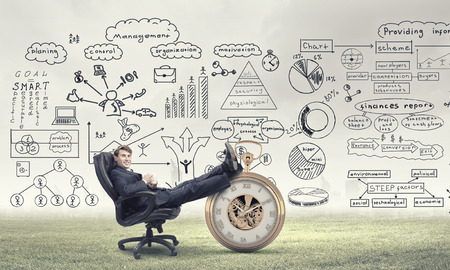 Young handsome businessman sitting in chair with cup in hands and his legs on watchの写真素材