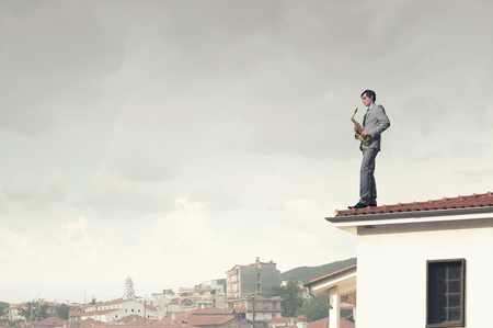 Young man in suit with saxophone in hands on house roofの写真素材