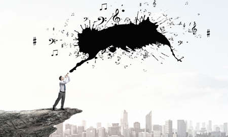 Young businessman on rock top playing pipeの写真素材