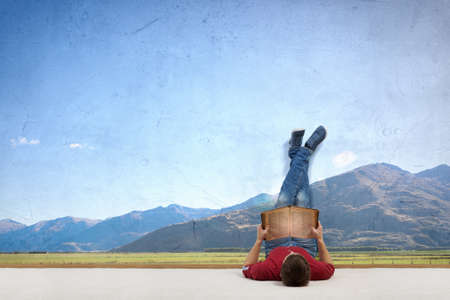 Young guy laying by the wall and reading bookの写真素材