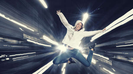 Young woman dancer jumping in spotlights on dark background