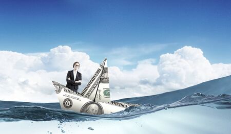 Businesswoman escapes from crisis on paper boat made of dollar banknoteの写真素材