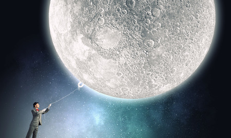 Young businessman in hat who obtains  moon with ropeの写真素材
