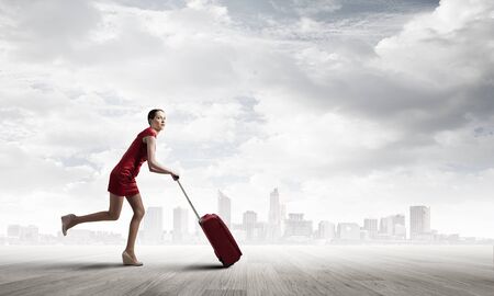 Young woman in red dress with red luggageの写真素材