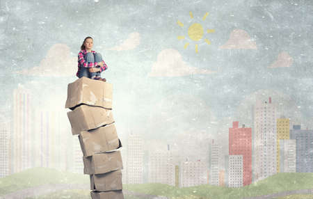 Smiling young woman sitting on stack of carton boxesの写真素材