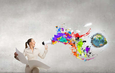 Portrait of young businesswoman with newspaper screaming in megaphone. Elements of this image are furnished by NASAの写真素材