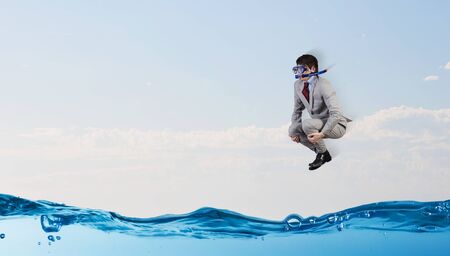 Young businessman in suit and diving mask jumping in waterの写真素材