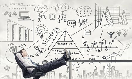 Smiling businessman sitting in chair with legs on tableの写真素材