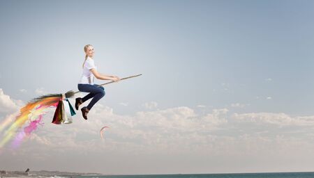 Happy young woman flying in sky on broomの写真素材
