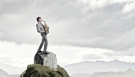 Young man on top of rock playing saxophoneの写真素材