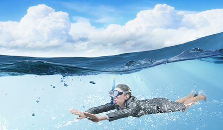Young businesswoman in suit and diving mask swimming under waterの写真素材