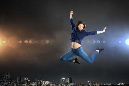 Young woman dancer jumping in spotlights on dark backgroundの写真素材