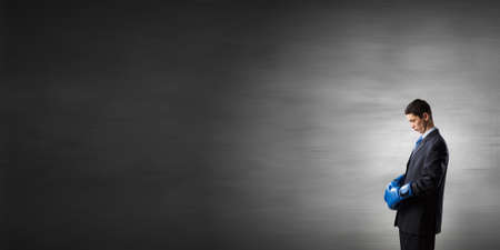 Young businessman in blue boxing gloves on dark backgroundの写真素材