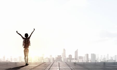 Back view of cheerful woman with hands up facing sunriseの写真素材
