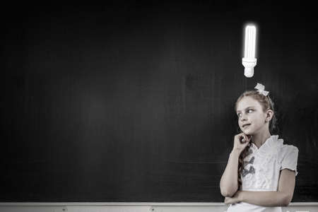 Cute thoughtful school girl and light bulb above her headの写真素材