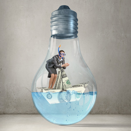 Young businesswoman in suit and diving mask jumping in lightbulb with waterの写真素材