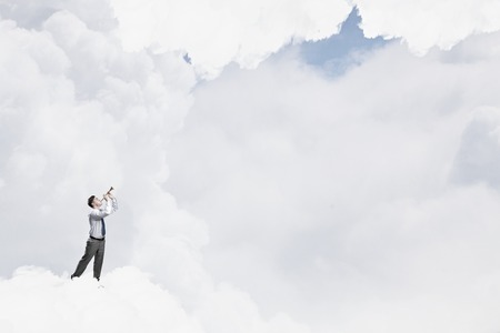 Young businessman on cloud in sky playing pipeの写真素材