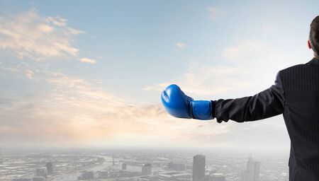 Back view of businessman in blue boxing gloves on city backgroundの写真素材