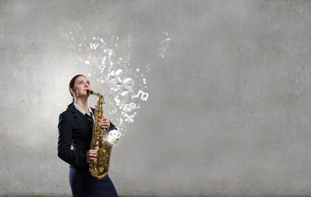 Young pretty woman in suit playing saxophoneの写真素材