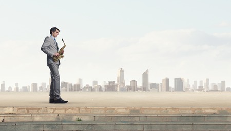 Young man in suit with saxophone in handsの写真素材