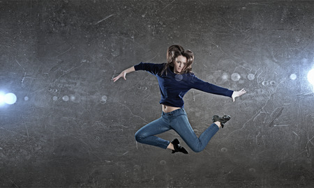 Young woman dancer jumping in spotlights on dark backgroundの写真素材