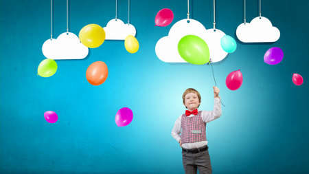 Little boy wearing red bowtie holding colorful balloonの写真素材