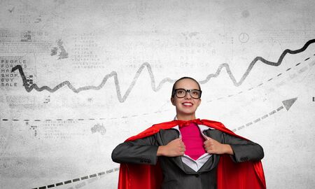 Young businesswoman in red cape acting like super heroの写真素材