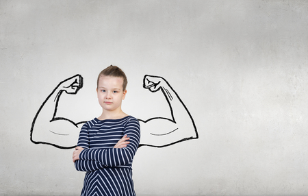 Cute kid girl with arms crossed on chest and drawn muscular handsの写真素材