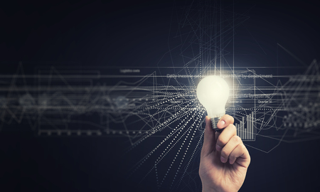 Human hand holding shining electric bulb and infographs on wallの写真素材