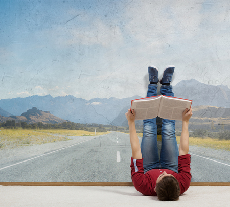 Young guy laying by the wall and reading bookの写真素材