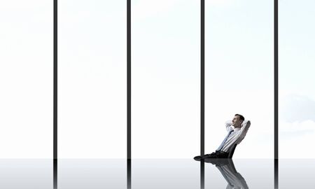 Relaxing businessman with crossed hands behind his head in officeの写真素材