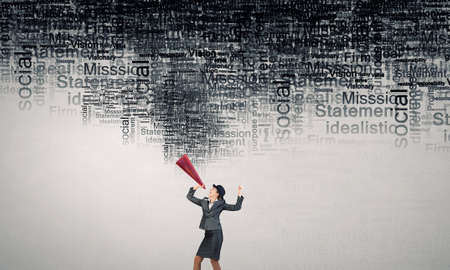 Young woman in suit and bowler hat screaming in paper trumpetの写真素材