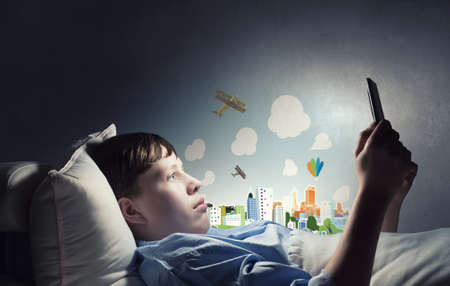 Teenage boy in pajamas lying in bed using tablet pcの写真素材