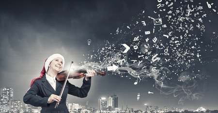 Woman in formal suit and Santa hat playing violinの写真素材