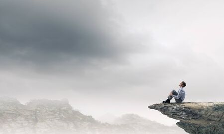 Young businessman sitting alone on rock topの写真素材