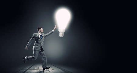 Young businessman running and catching glowing light bulbの写真素材