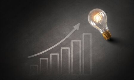 Glowing glass light bulb hanging from above and business sketches at dark backgroundの写真素材