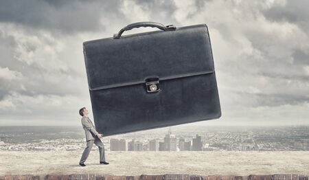 Young determined businessman carrying big heavy suitcaseの写真素材