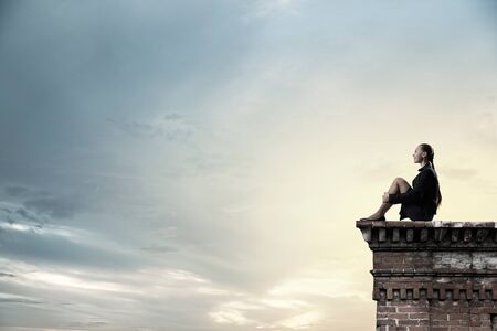 Bored young businesswoman sitting alone on building top