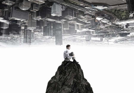 Young thoughtful businessman sitting alone on rock topの写真素材