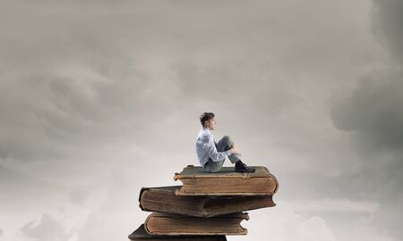 Young businessman sitting alone on pile of old booksの写真素材