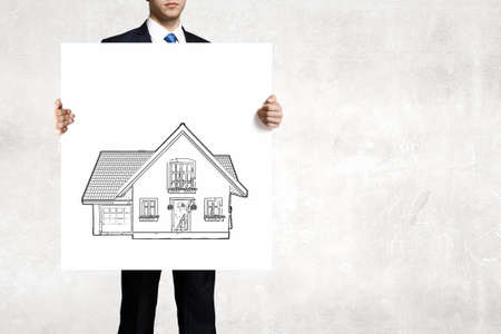 Businessman in suit holding placard with house symbolの写真素材