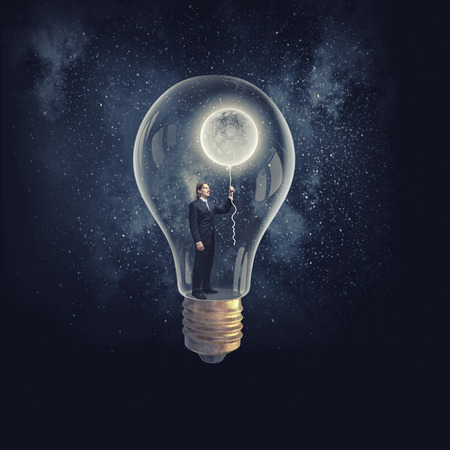 Businessman inside of glass light bulb with moon balloon on dark backgroundの写真素材