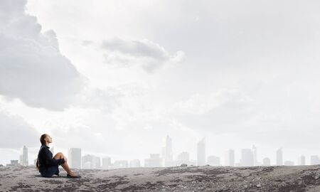 Thoughtful young businesswoman sitting alone on rock topの写真素材