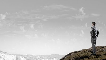Rear view of confident businessman standing on rock topの写真素材