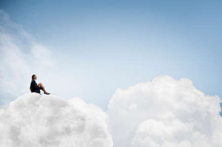 Thoughtful young businesswoman sitting alone on cloud high in skyの写真素材